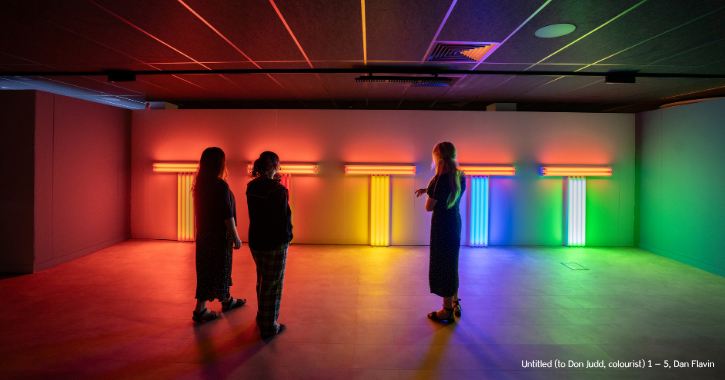Group of three woman stood admiring a colourful light art installation at the Light Durham.